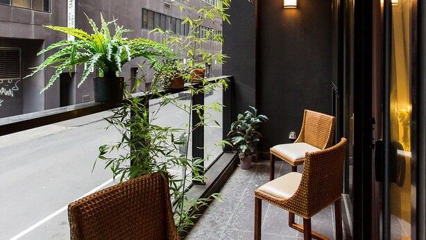 A balcony with wicker chairs and potted plants, overlooking a city street. - Anchor on Little Collins - Southern (Melbourne)