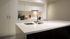 A modern kitchen with white cabinetry, a white countertop, and a stainless steel sink. - Anchor on Little Collins - Southern (Melbourne)