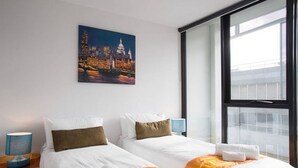 A hotel room with two beds, a painting of a cityscape, a window with a view, and a nightstand with a lamp. - Anchor on Little Collins - Southern (Melbourne)