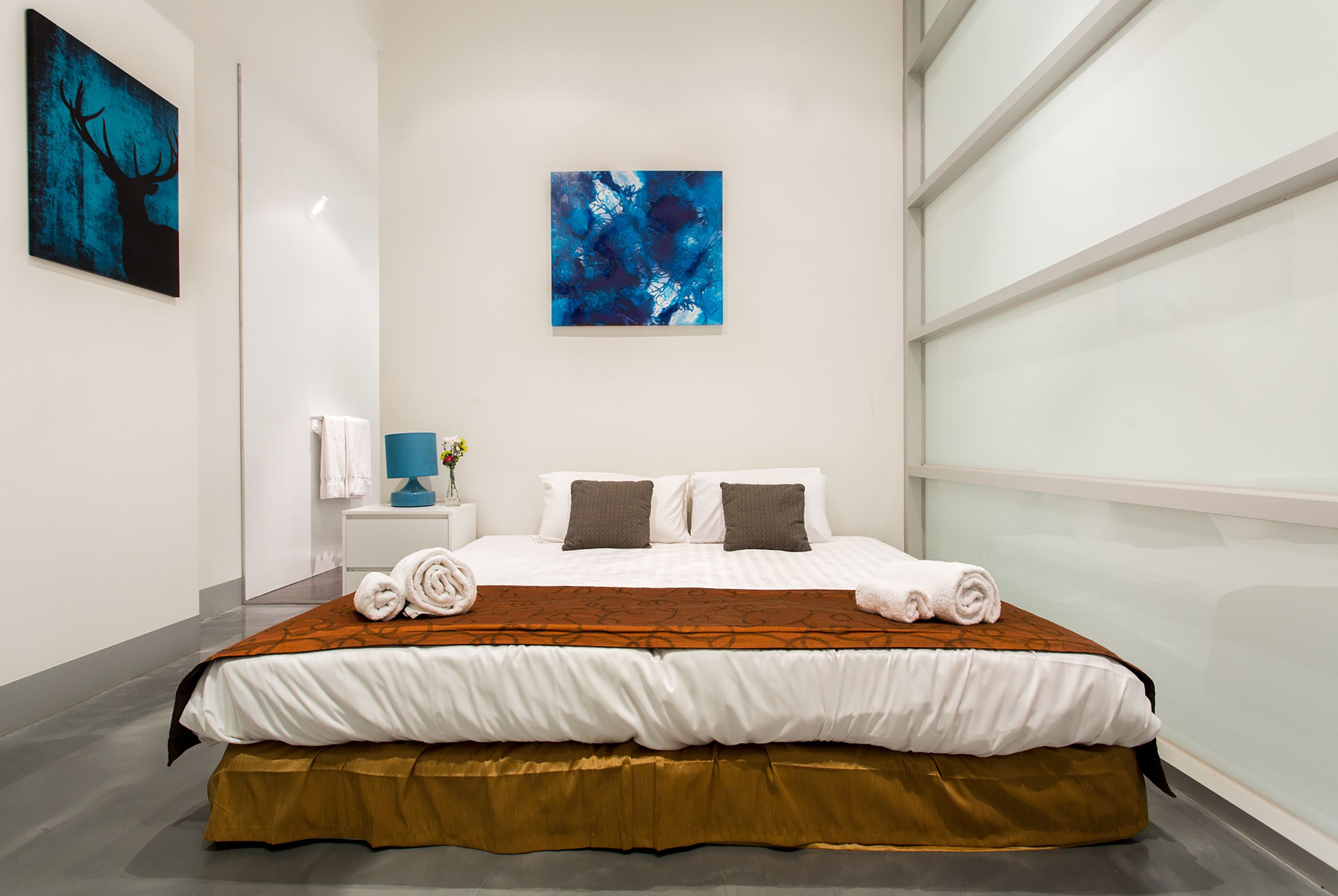 A modern hotel room with a large bed, white walls, and artwork.