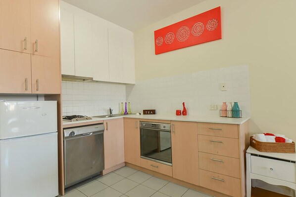 A kitchen with white cabinets, a stove, an oven, and a dishwasher. There is a red artwork on the wall and a basket on the counter. - Anchor on Elizabeth (Melbourne)