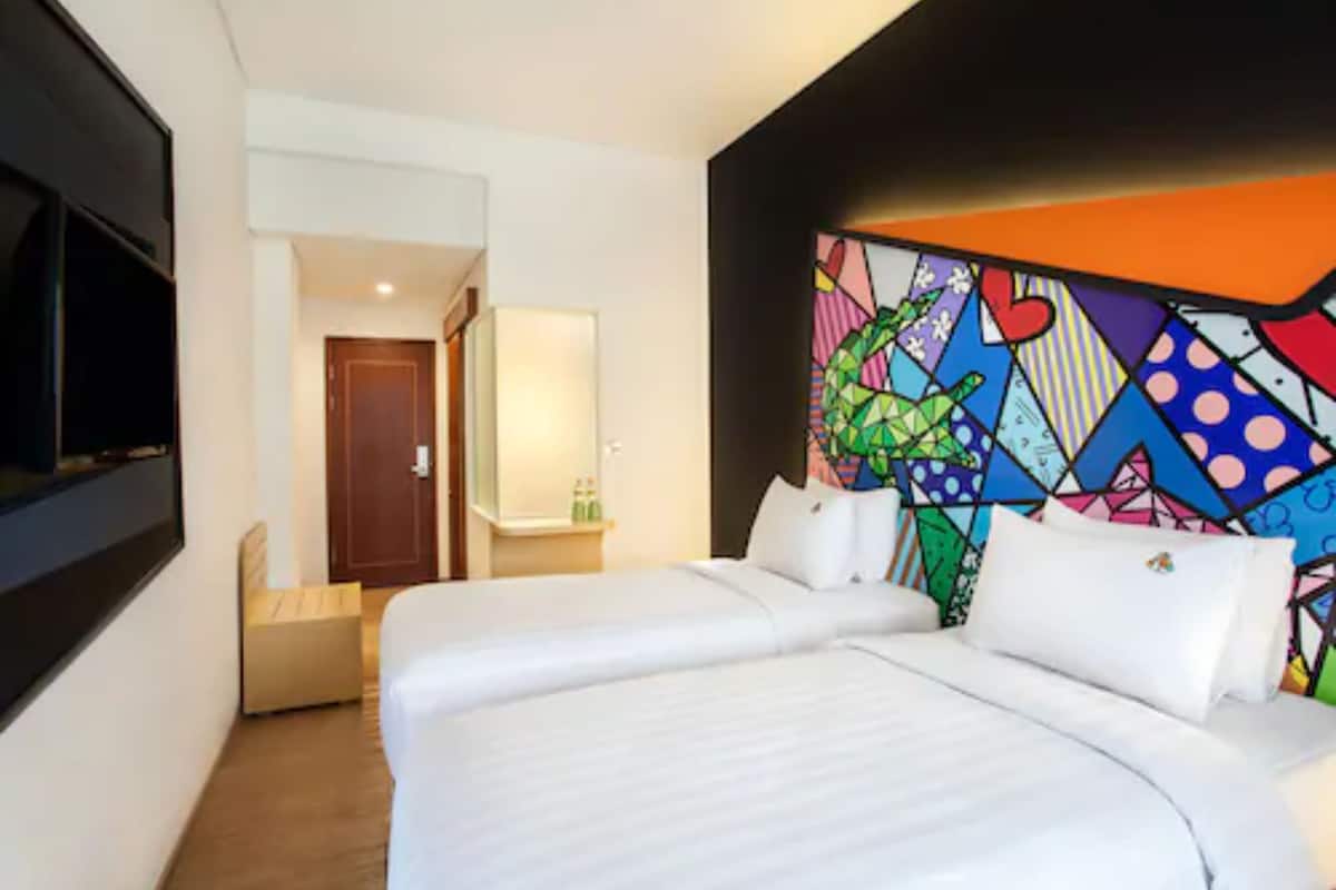 A hotel room with two beds, a TV, and a colorful wall mural.