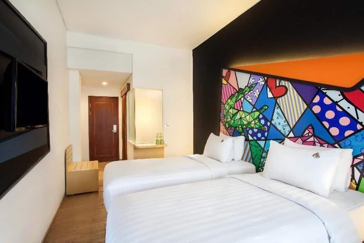 A hotel room with two beds, a TV, a mirror, and a colorful geometric wall design.