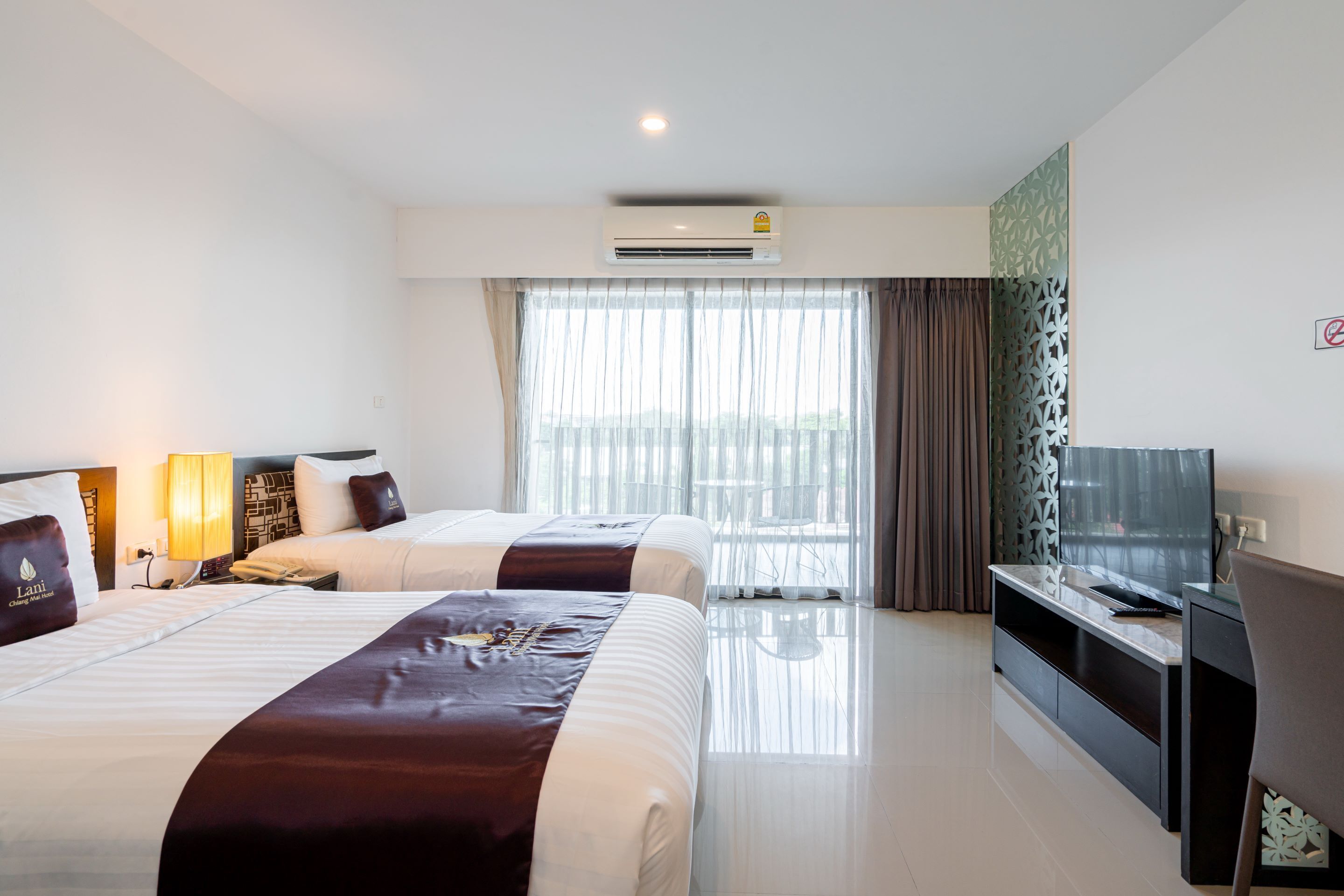 A hotel room with two beds, a TV, and a large window with curtains.