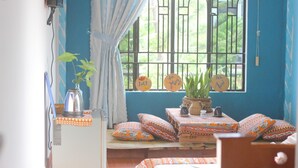A room with a window, a bed, a table with a plant, and a wall clock. - Longan Homestay (Da Nang)