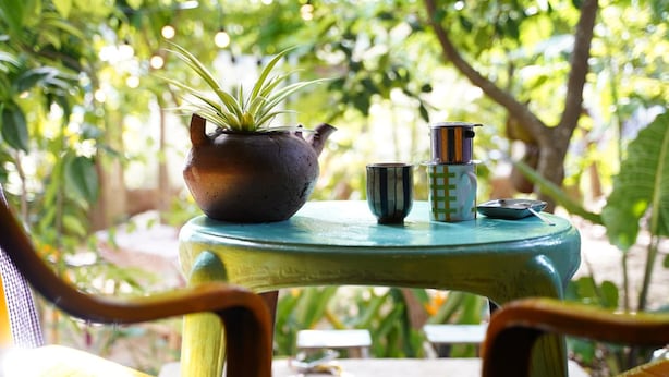 A small round table with a potted plant, a striped mug, and a metallic container. - Longan Homestay (Da Nang)