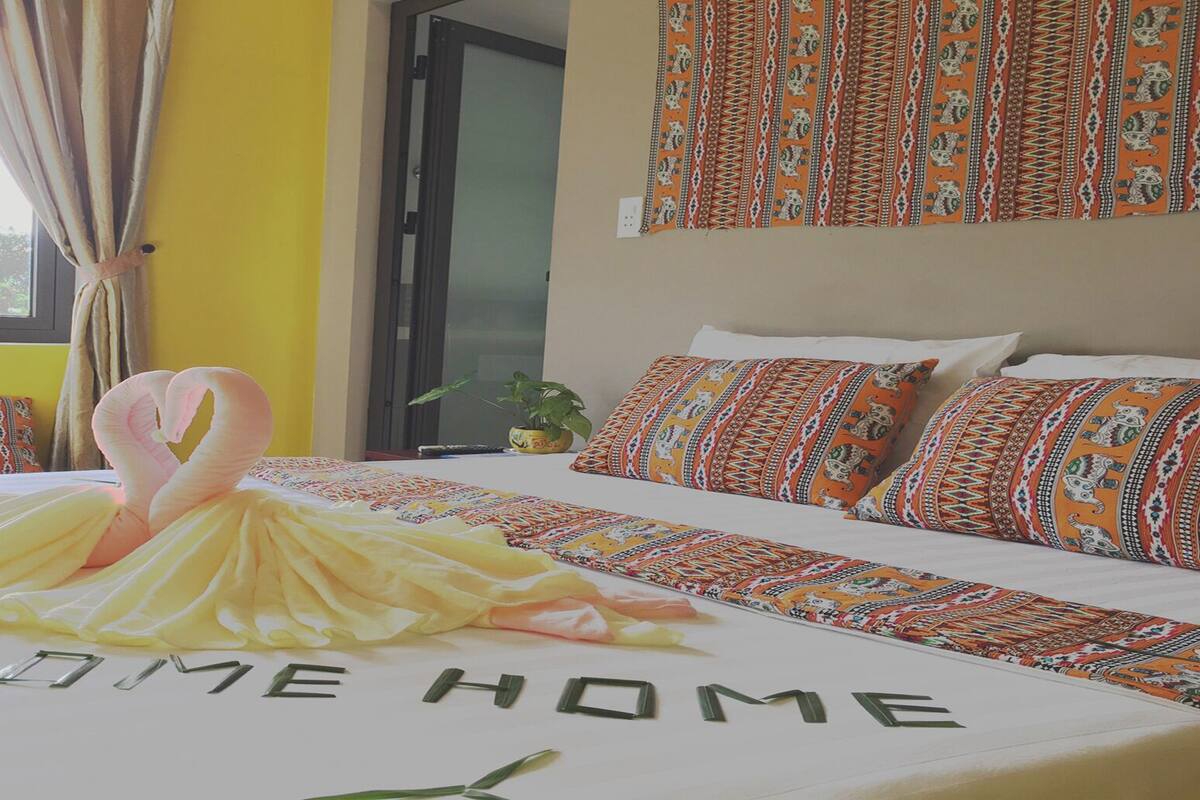 A hotel room with a bed featuring a 'WELCOME HOME' sign, a heart-shaped decoration, and patterned pillows.