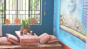 A room with a view of a boat on water through a window, a small table with a plant, and colorful pillows. - Longan Homestay (Da Nang)