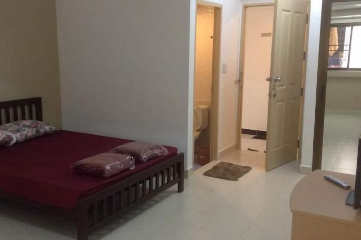 A bedroom with a wooden bed, a red bedspread, and two pillows. There is a door leading to a bathroom.