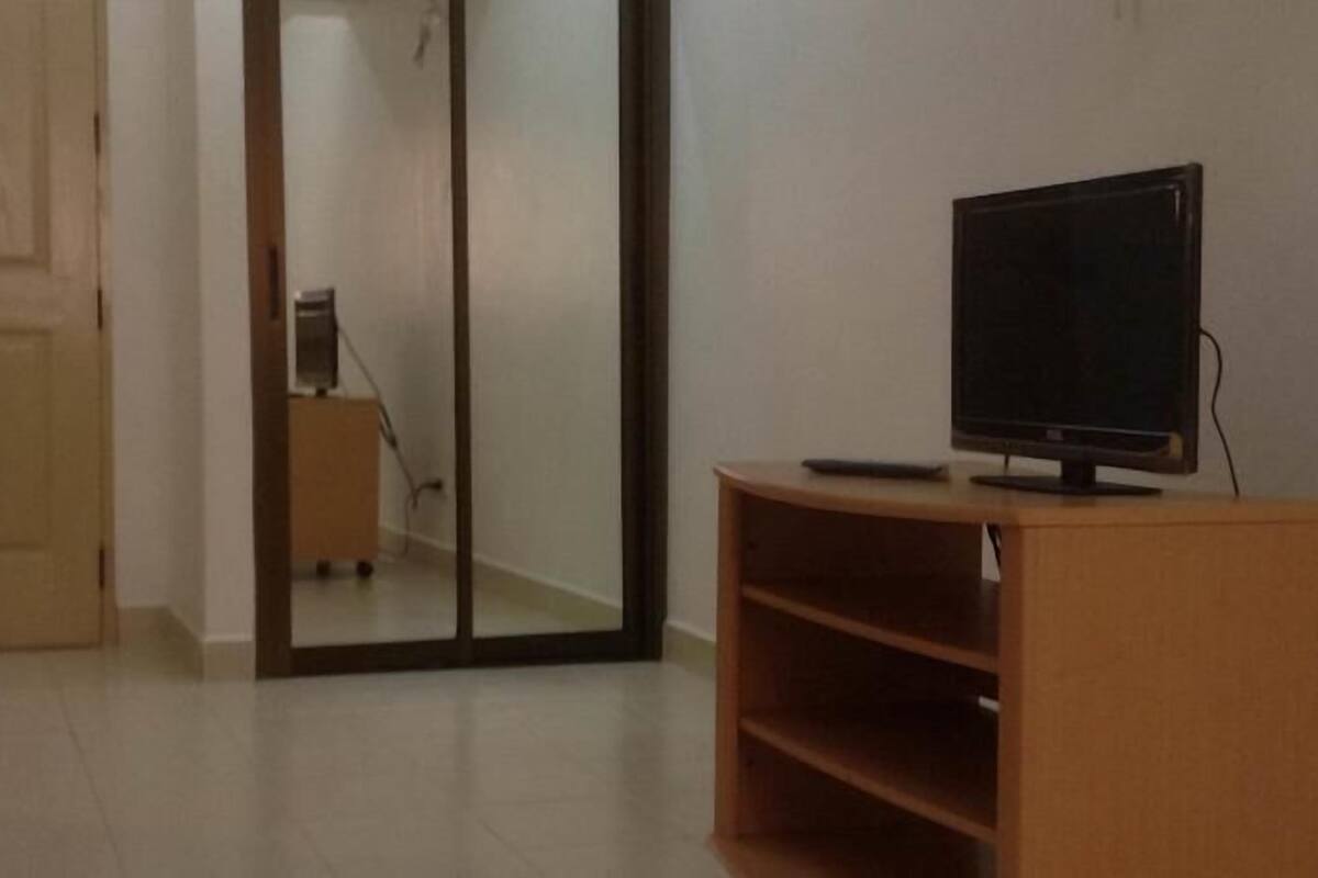 A room with a wooden door, a sliding glass door, a television on a wooden stand, and a tiled floor.