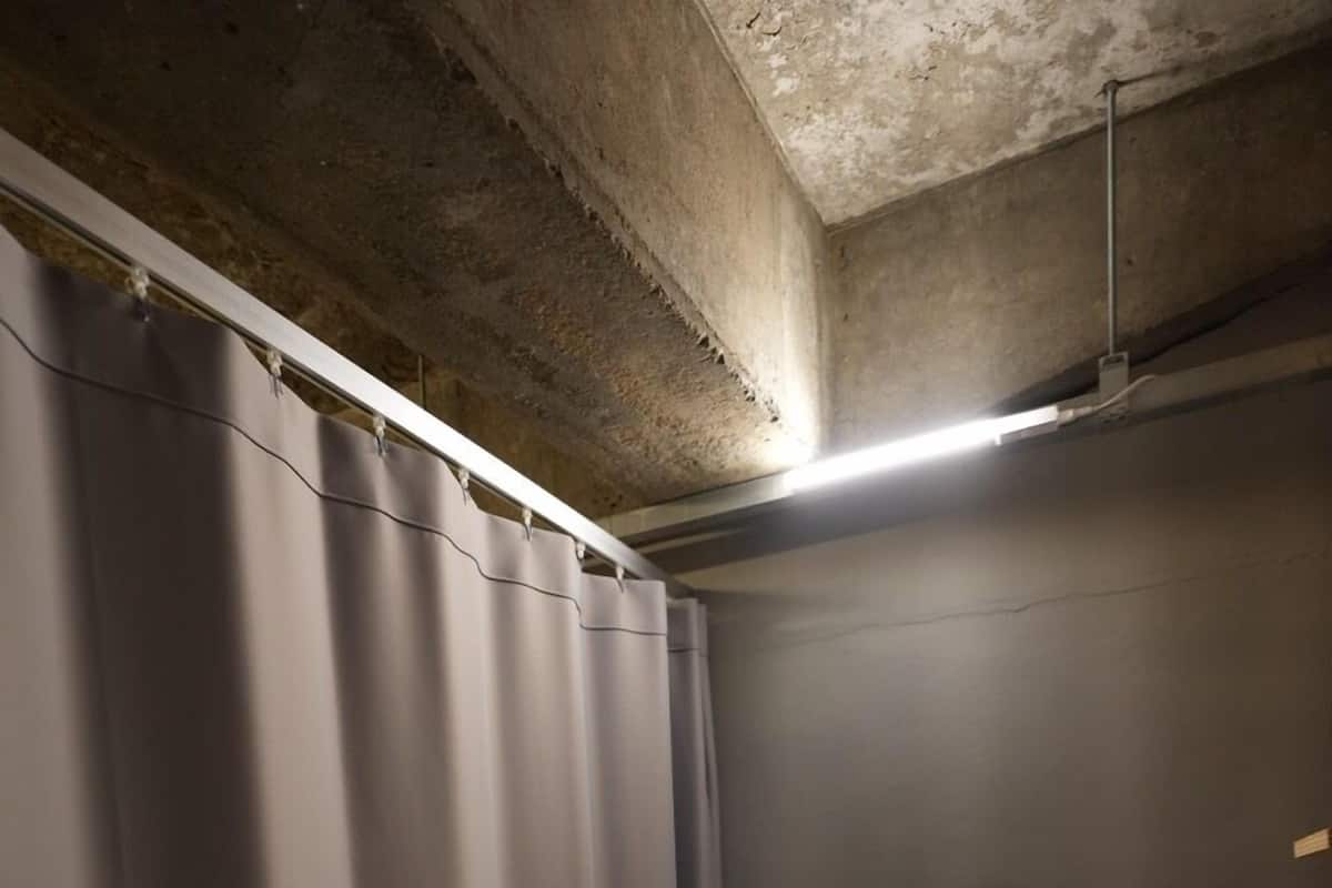Un lit simple avec un cadre en métal, un oreiller blanc et un rideau gris.