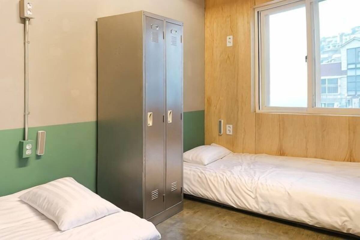 Une chambre avec deux lits, une armoire, une fenêtre et un radiateur fixé au mur.