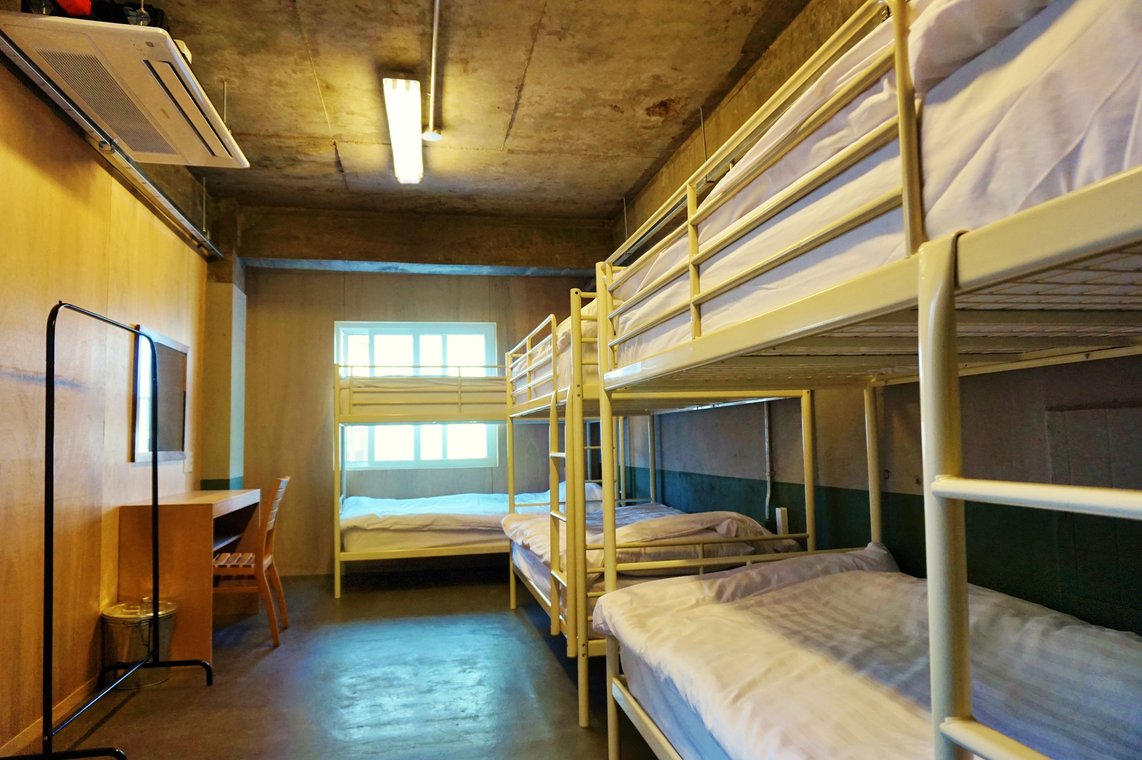 Un dormitorio con literas, un escritorio y una ventana que deja entrar luz natural.