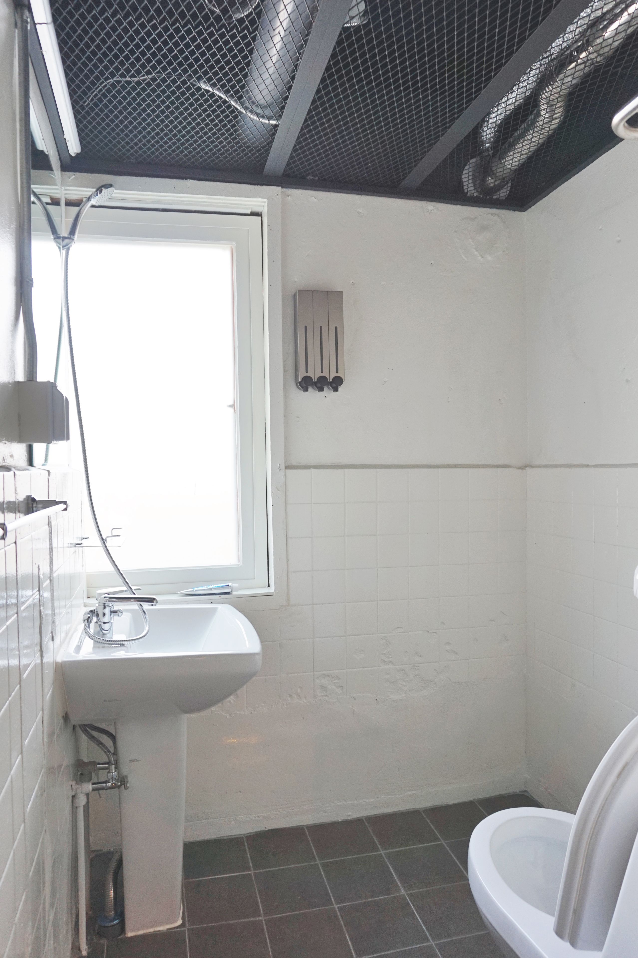 Une salle de bain avec un lavabo blanc, des toilettes et une fenêtre.