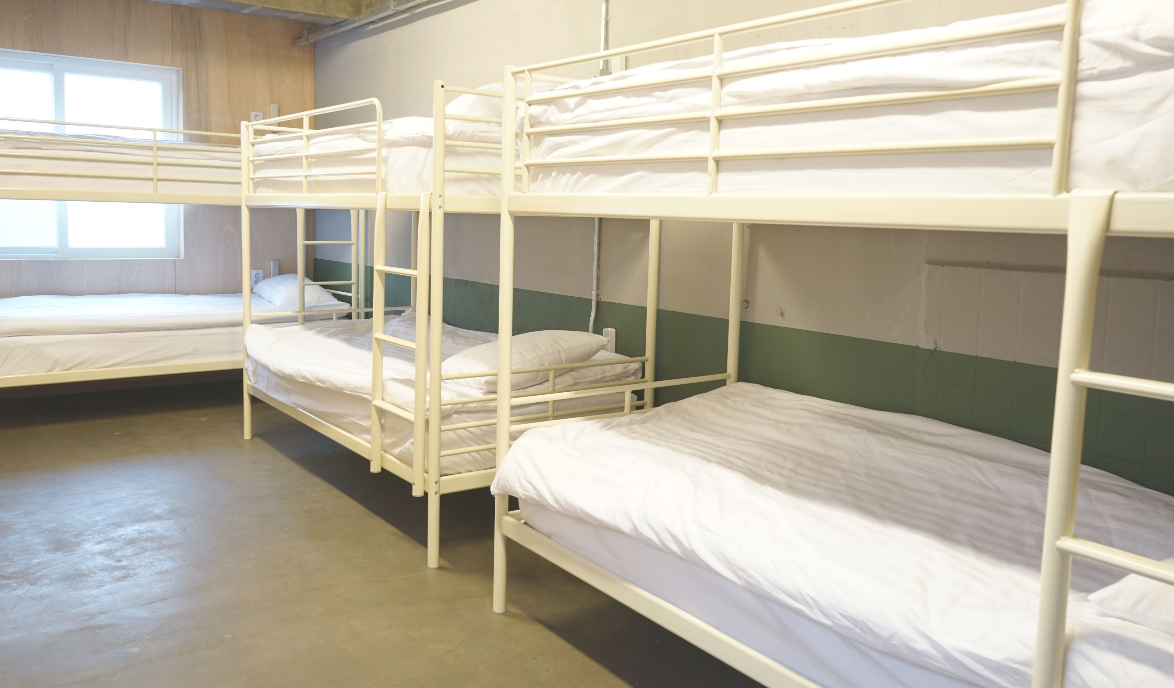 Une chambre de dortoir avec des lits superposés, une fenêtre et un mur vert.