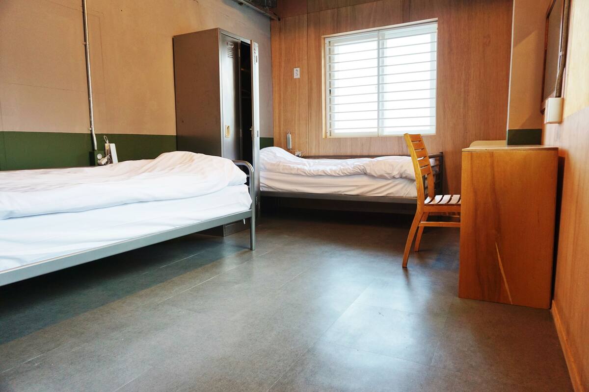 Une chambre avec deux lits, une chaise en bois et un bureau.