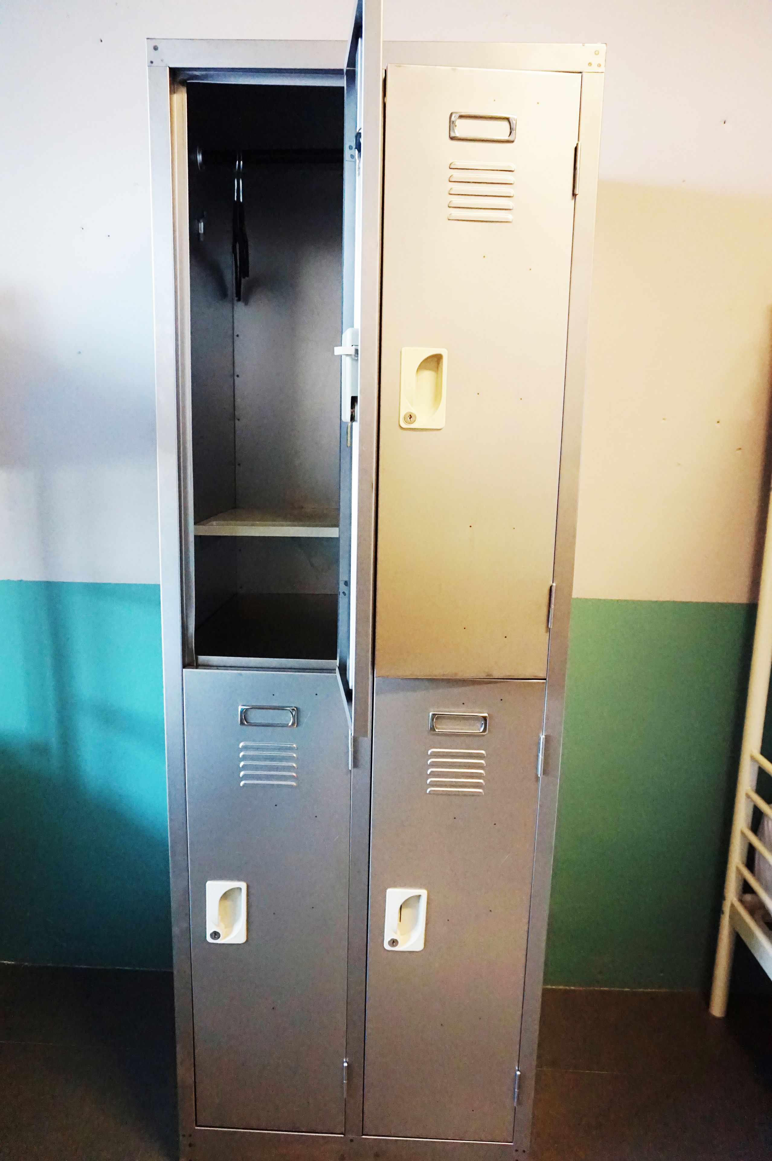 A set of metal lockers with a handle and a small shelf, against a wall with a teal and white color scheme.