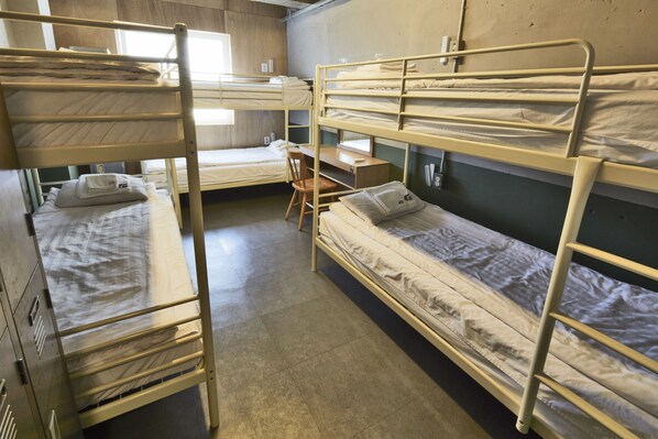 A dormitory room with bunk beds, a desk, and a chair.
