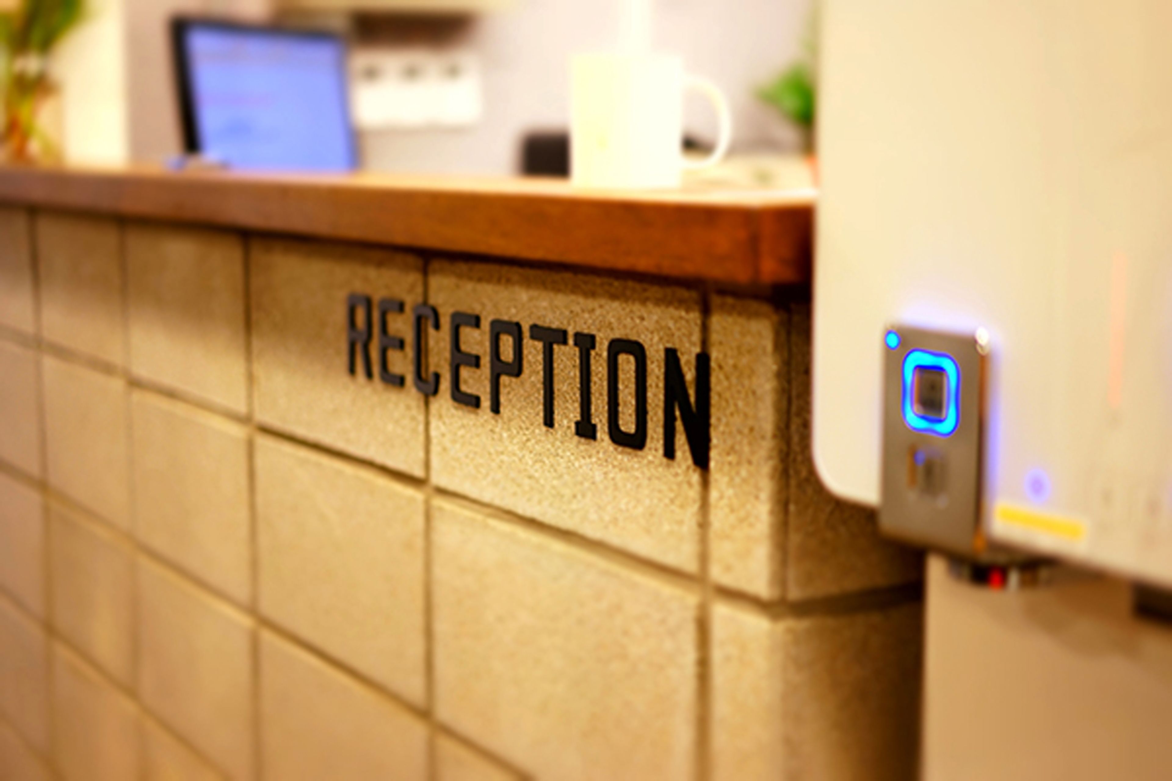 A reception area with a tiled wall and a digital device on the right.