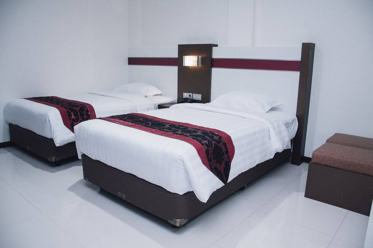 A hotel room with two beds, a nightstand, and a bench.