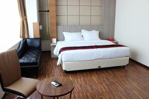 Ein Hotelzimmer mit einem Bett, einer schwarzen Ledersofa, einem runden Holztisch und einem roten Mülleimer.