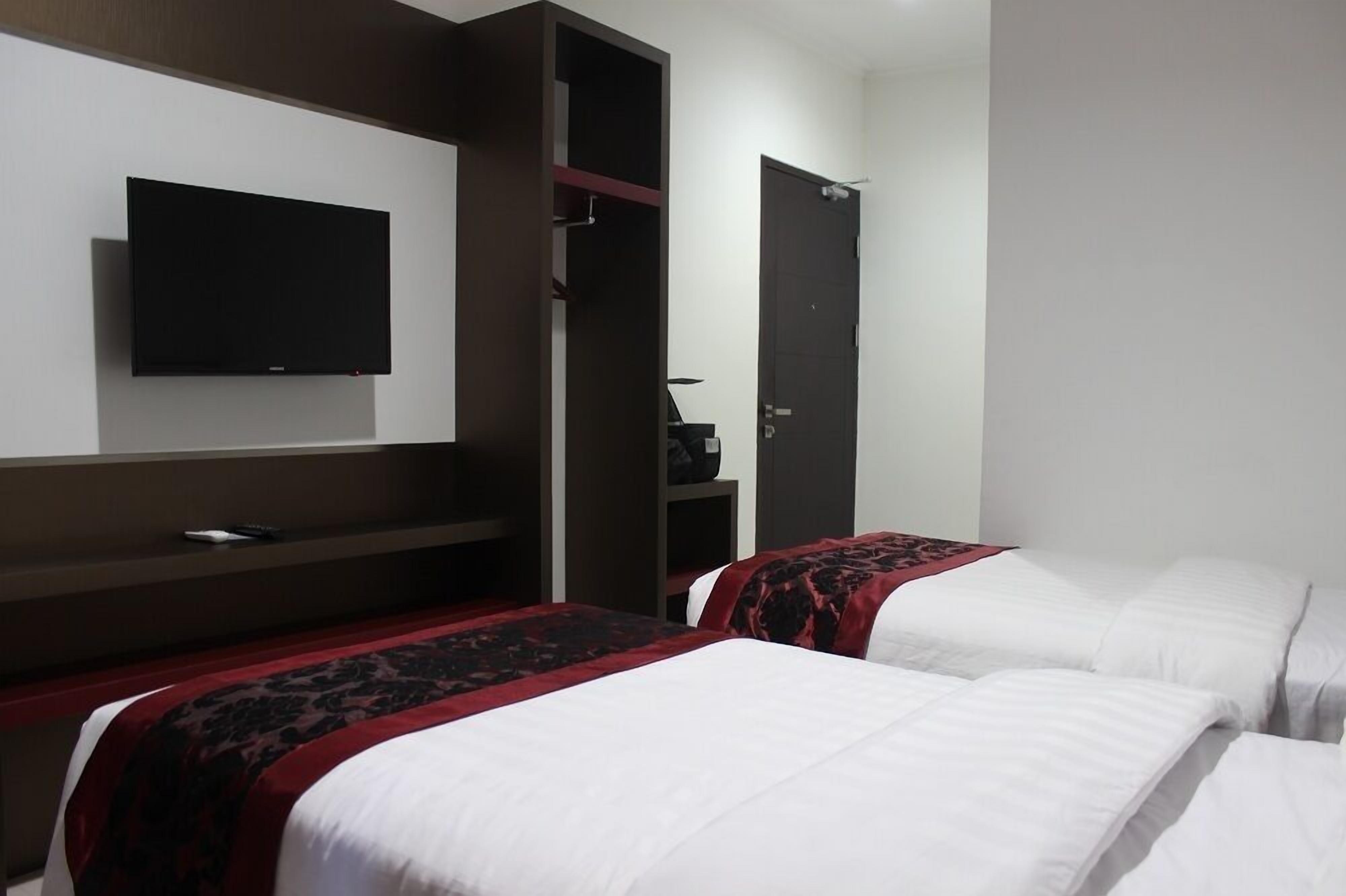 A hotel room with two beds, a TV mounted on the wall, and a wardrobe.