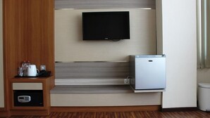 A hotel room with a flat-screen TV mounted on a wall, a mini-fridge, and a small cabinet with a microwave. - Idea's Hotel (Bandung)