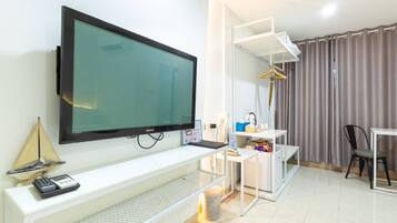 Habitación de hotel moderna con una televisión de pantalla plana grande montada en la pared, un escritorio pequeño con una computadora portátil, una silla y un perchero.