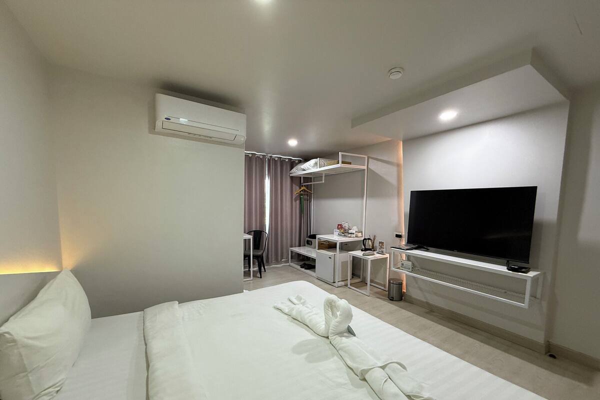 A hotel room with a neatly made bed, a desk with a chair, a television, and a wardrobe.
