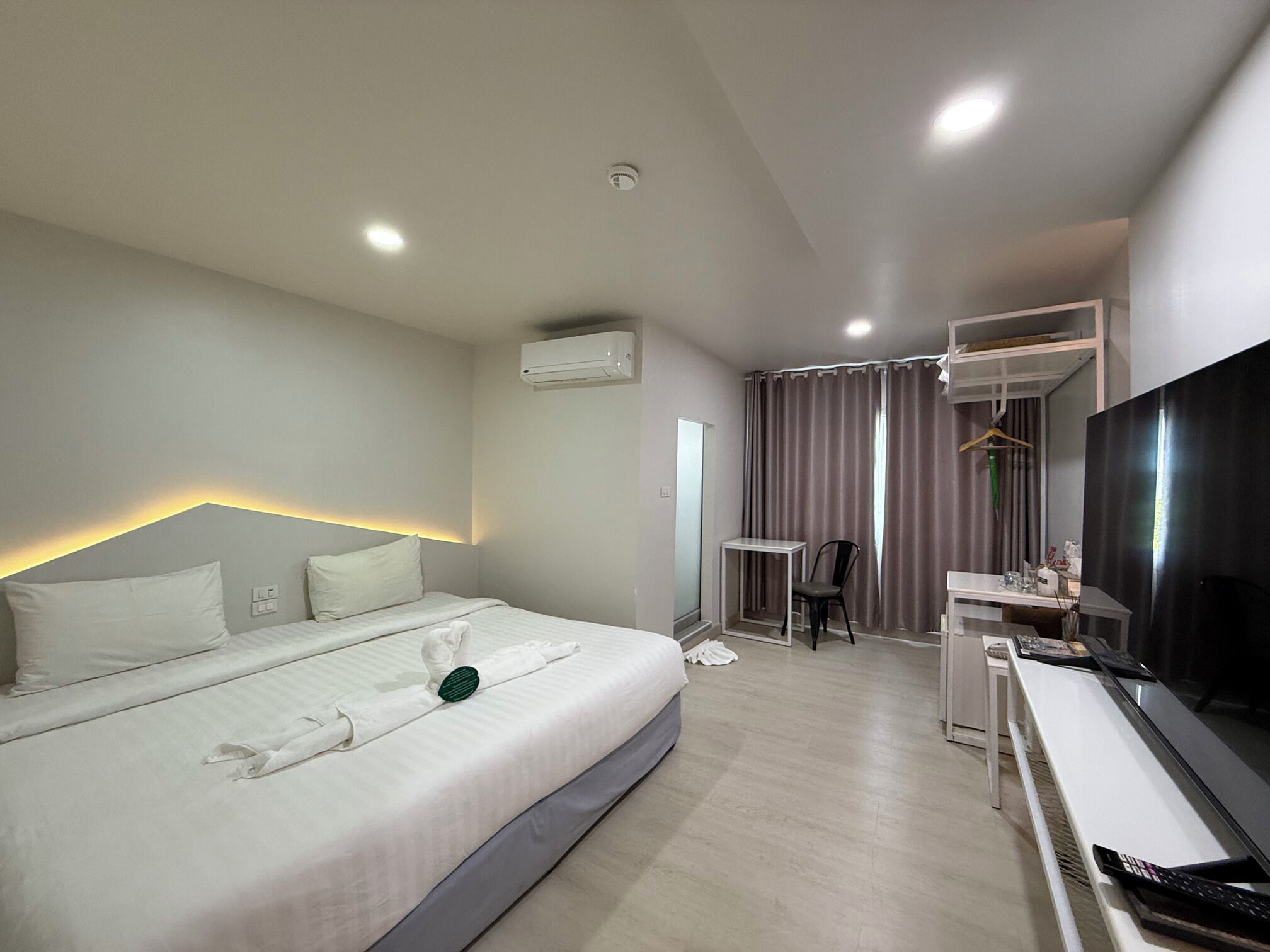 A hotel room with a bed, a desk, a chair, a TV, and an air conditioning unit.
