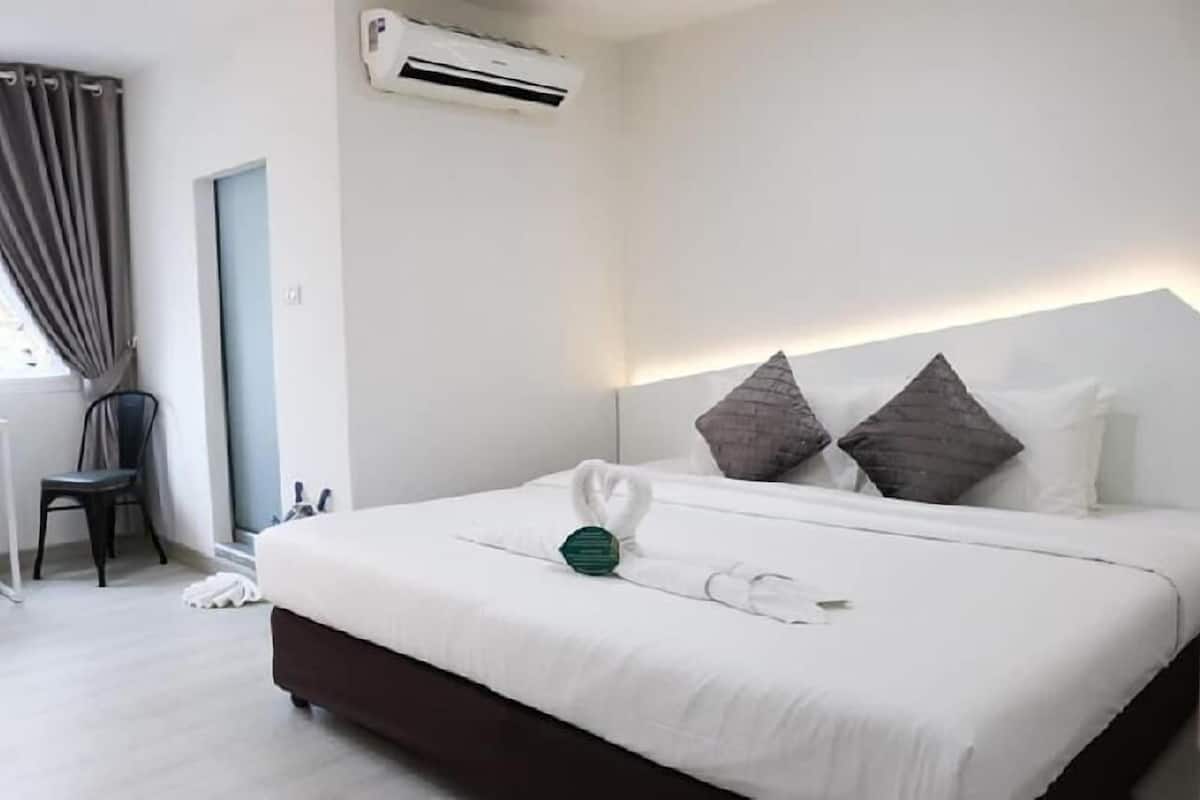 A hotel room with a bed, a chair, an air conditioning unit, and a window with curtains.