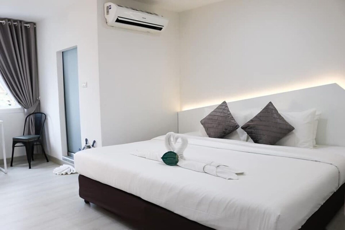 A hotel room with a bed, a chair, an air conditioning unit, and a window with curtains.