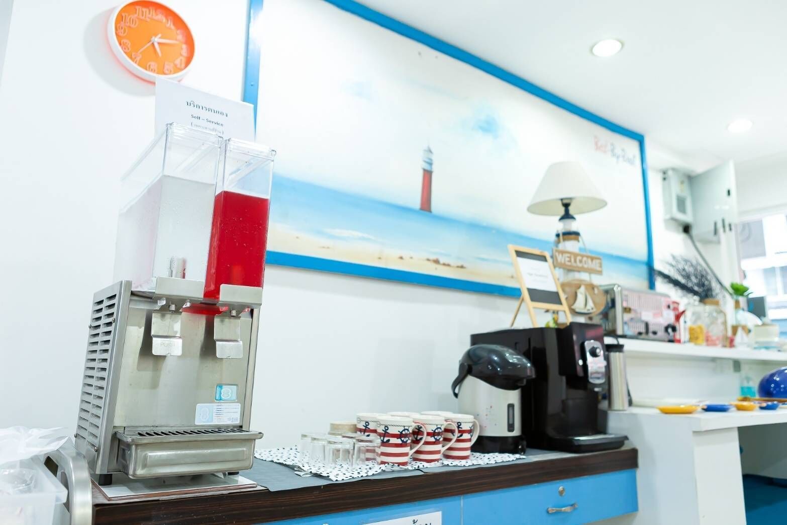 A coffee station with a coffee machine, a red beverage dispenser, and a clock on the wall.