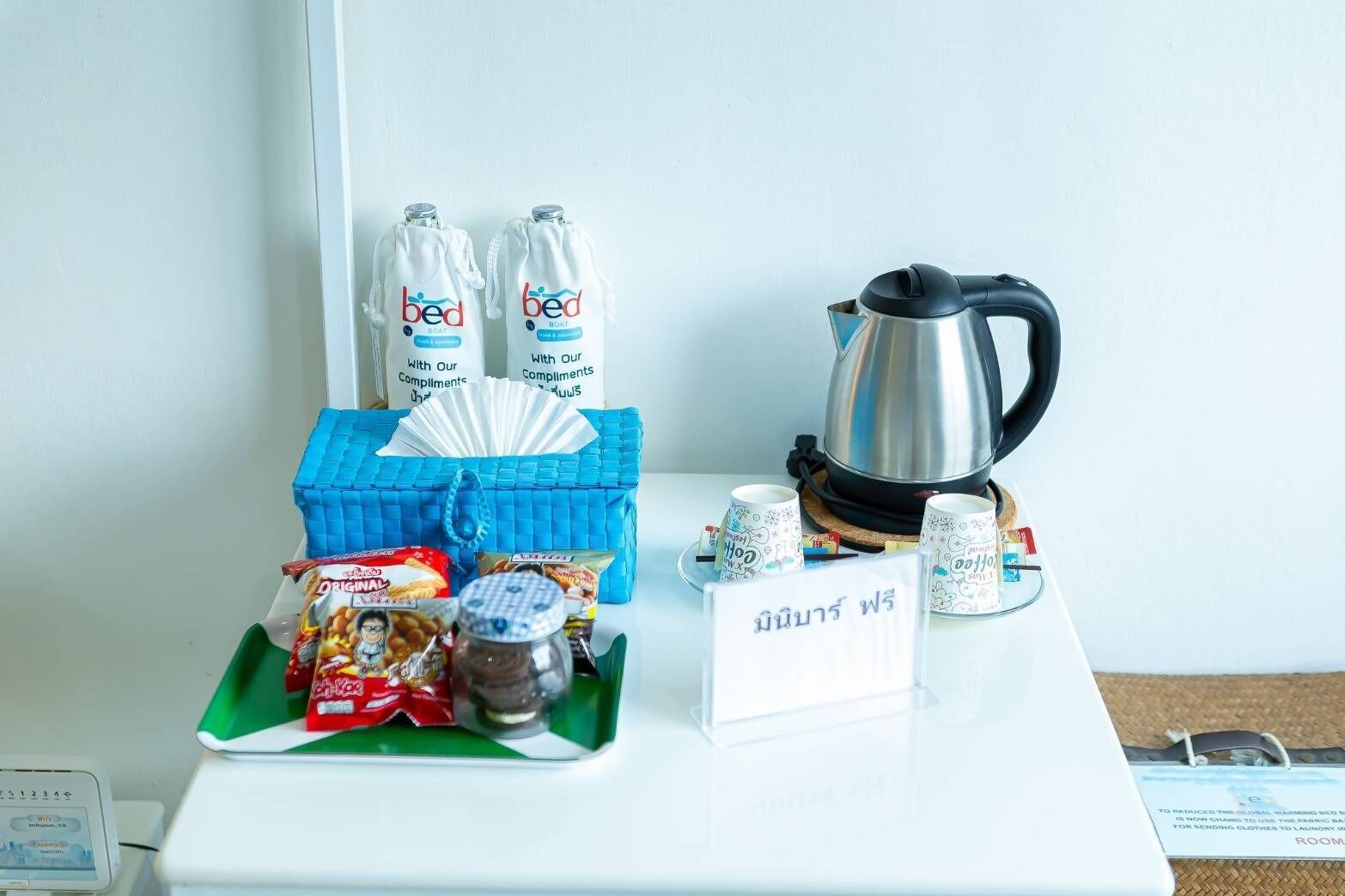 A hotel room with a table set with snacks, a kettle, and a sign with Thai text.