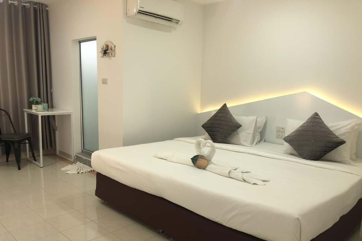 A hotel room with a bed, a desk, and an air conditioning unit.