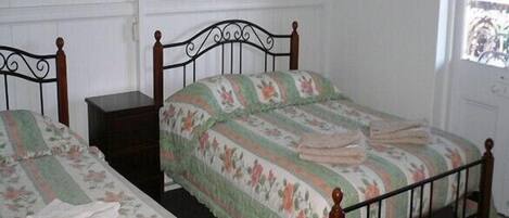 Dos camas individuales con estructura de madera y ropa de cama estampada en una habitación con paredes blancas y una ventana.