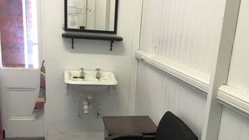 A small, compact bathroom with a white sink, a mirror, and a black chair.