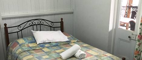 A single bed with a quilt, a white pillow, and a rolled towel.