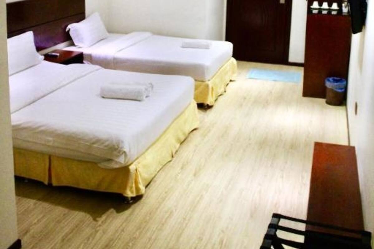 Habitación de hotel con dos camas individuales, piso de madera, ventilador de techo, una puerta y un pequeño escritorio con silla.
