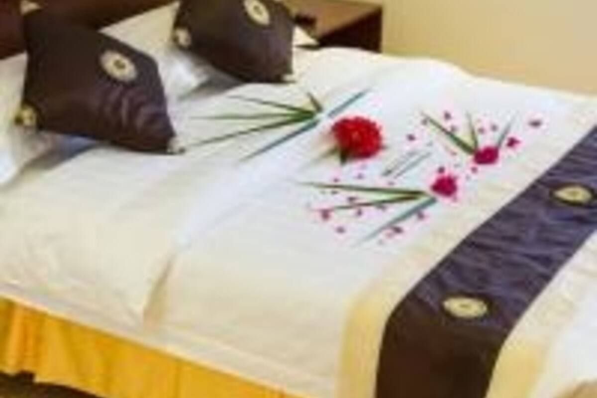 Una cama bien hecha con cubrecama blanco y marrón oscuro, dos almohadas decorativas y un arreglo floral.