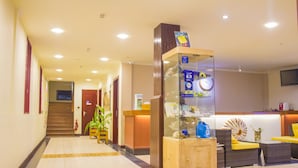A hotel reception area with a reception desk, a glass display case, a staircase, and a seating area with yellow cushions. - WhiteShell Island Hotel & Spa (Maafushi)