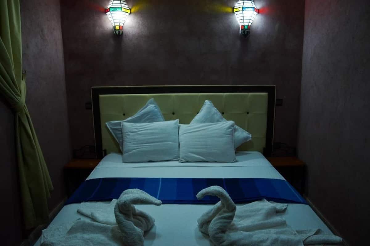 A hotel room with a bed, two wall-mounted lights, and a blue bedspread.