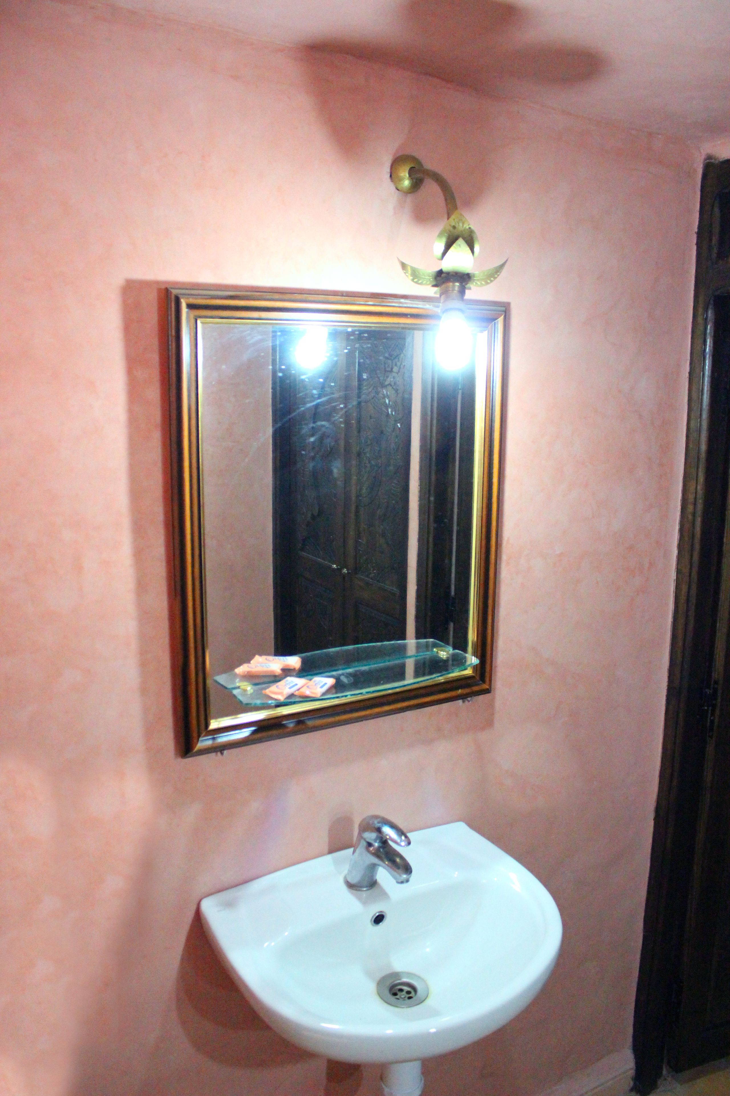 Een badkamer met een witte wastafel, een spiegel met gouden lijst, en een lamp boven de spiegel.