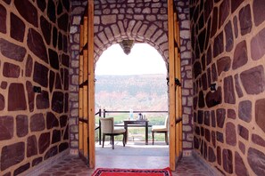 An arched stone doorway leading to a balcony with a table and chairs, overlooking a mountainous landscape. - Riad Aslda (Asni)
