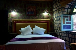 A bed with white bedding and a purple blanket, a stone wall, and a window with decorative iron bars.