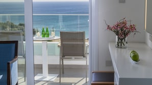 Varanda com vista para o oceano, uma mesa com garrafas e copos, uma cadeira e um vaso com flores.