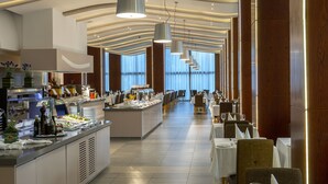 Uma área de refeições moderna em hotel, com buffet, longas mesas e uma ilha central.