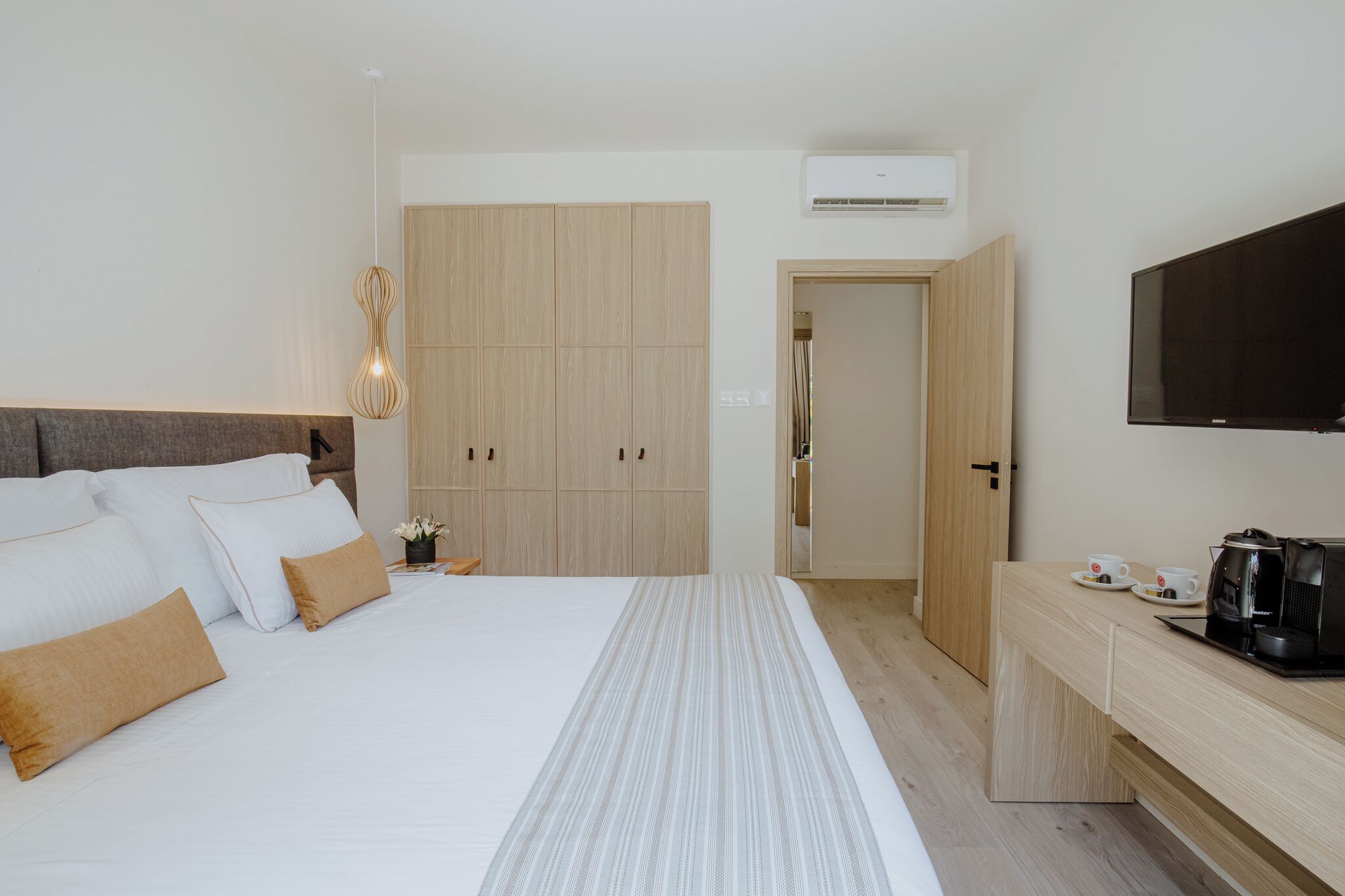 A modern hotel room with a large bed, wooden wardrobe, a television, and a coffee maker.