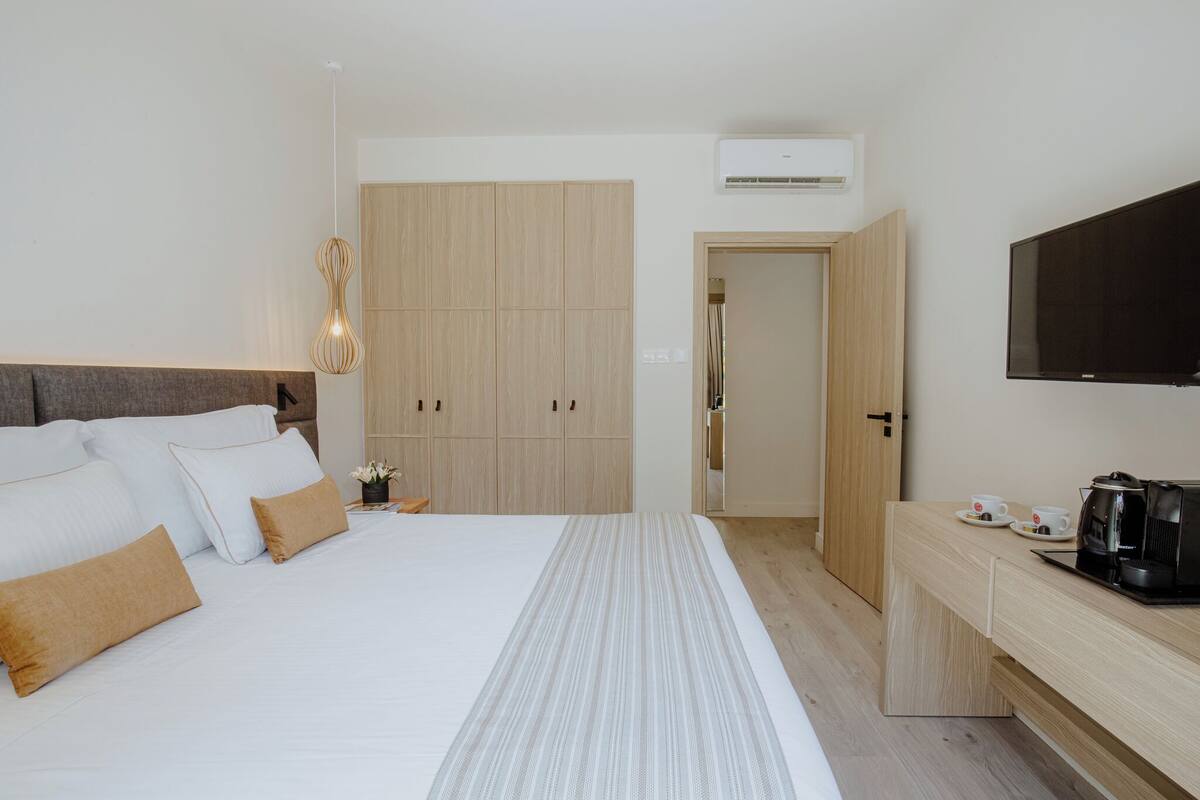 Moderni hotellihuone, jossa on suuri sänky, puinen vaatekaappi, televisio ja kahvinkeitin.