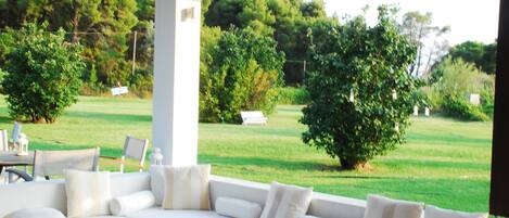 A modern outdoor seating area with a white sofa and a round table, overlooking a well-maintained lawn and trees.
